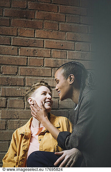Romantic gay couple looking at each other by brick wall