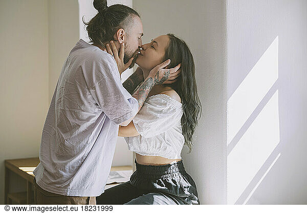 Romantic hipster couple kissing in front of wall