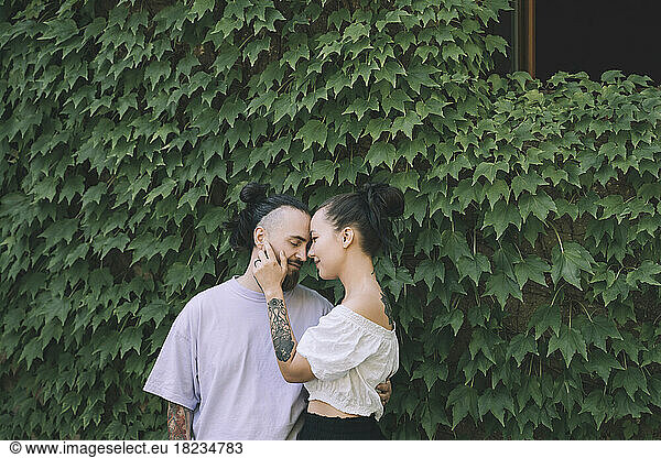 Romantic hipster couple standing in front of green ivy plants