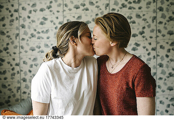 Romantic lesbian couple kissing against wall at home