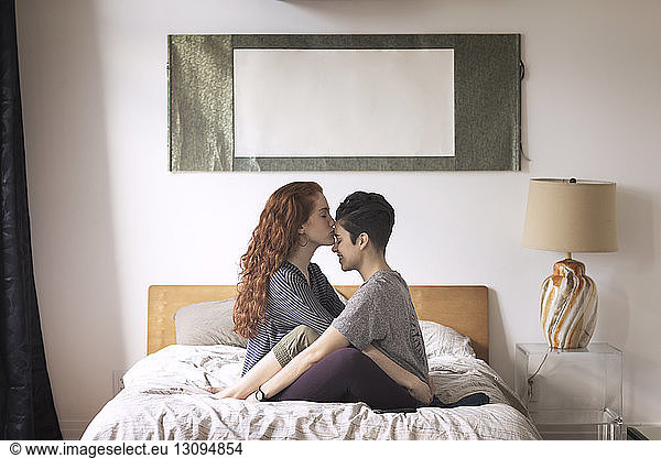 Romantic lesbian kissing on girlfriend's forehead while sitting on bed at home