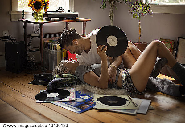 Romantic man lying with woman holding vinyl record on floor at home