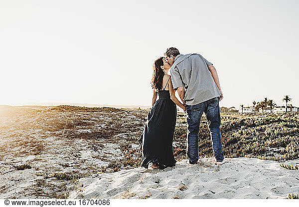 Romantic mid-40's couple kissing while standing on sand dune at beach