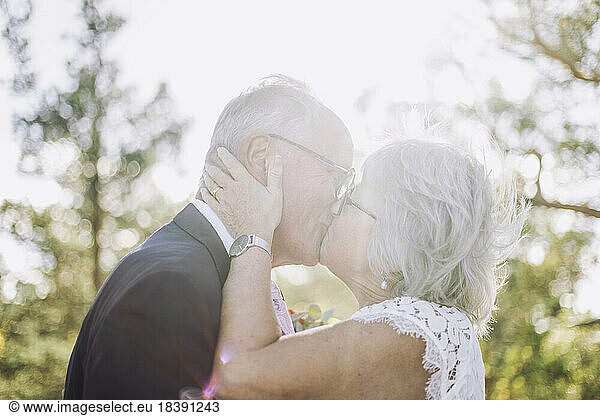 Romantic newlywed senior bride kissing groom on mouth at wedding during sunny day