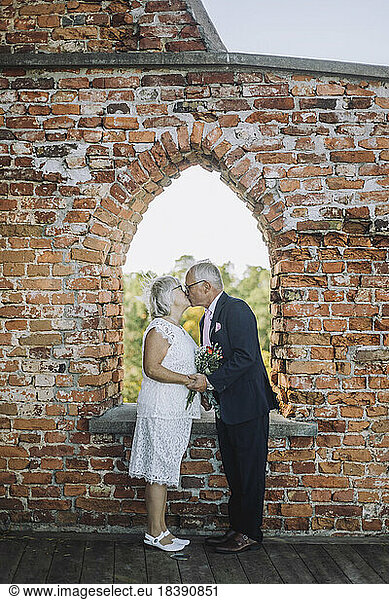 Romantic senior couple kissing on mouth by window during wedding