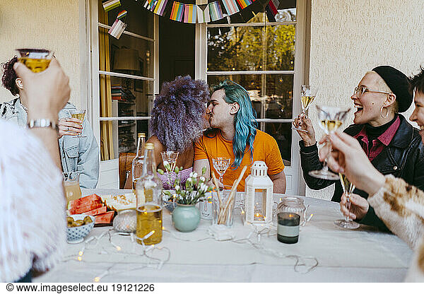 Romantic transwoman kissing gay friend during dinner party in back yard
