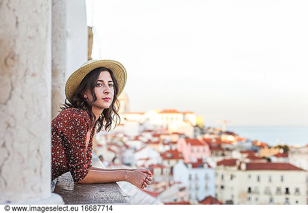 Romantic woman in a straw hat looking over a rooftop view of Lisbon