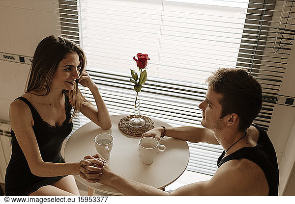 Romantisches junges Paar mit roter Rose am Küchentisch sitzend