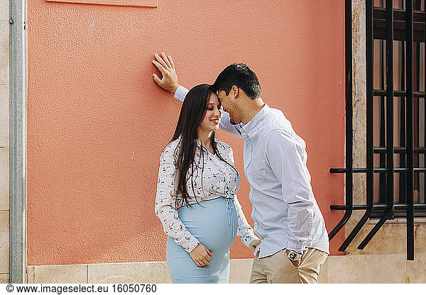 Romantisches schwangeres Paar steht Kopf an Kopf vor einer rosa Wand in der Stadt