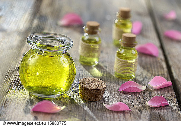 Rose flower petals with aromatherapy essential oil glass bottle isolated on wooden  background  copy-space