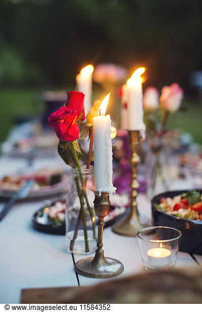 Roses in vase and lit candles amidst food on table at garden party