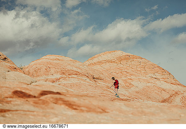 rot gekleidete Wanderin geht auf eine rot-weiß versteinerte Sanddüne