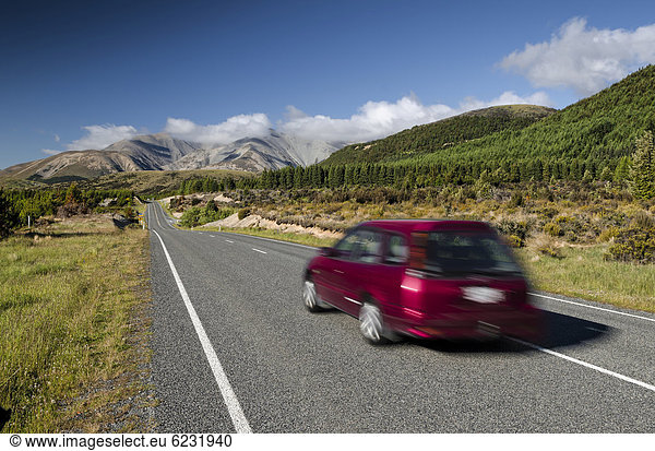 Rotes Auto fährt auf Landstraße  Linksverkehr  Arthur's Pass Road  Südinsel  Neuseeland  Ozeanien