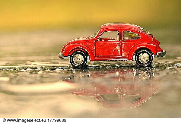 Rotes Spielzeugauto  VW Käfer mit Spiegelung auf regennasser Straße