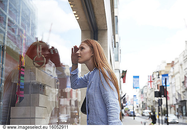 Rothaarige Frau  die ihre Augen abschirmt  während sie durch ein Schaufenster in der Stadt schaut