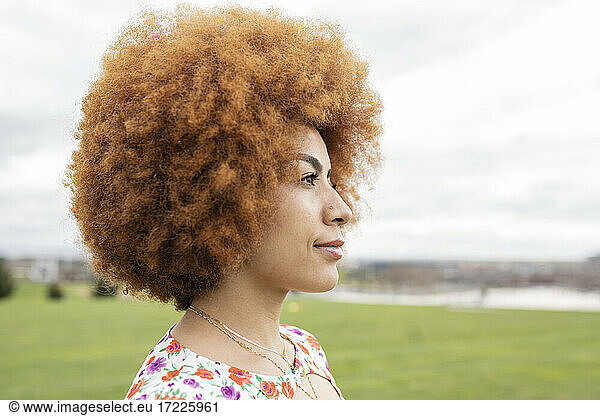 Rothaarige Frau mit Afrofrisur schaut im Park weg