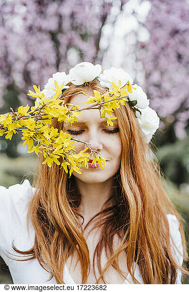 Rothaarige Frau mit geschlossenen Augen  die ein Blumen-Diadem trägt und einen Strauß gelber Blumen hält