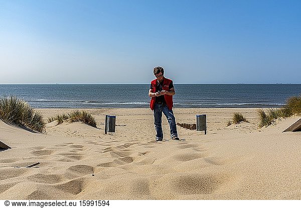 Rotterdam  Niederlande. Reifer erwachsener Mann bei der Arbeit mit seinem Smartphone auf einer Corona Deserted  Maasvlakte Beach.