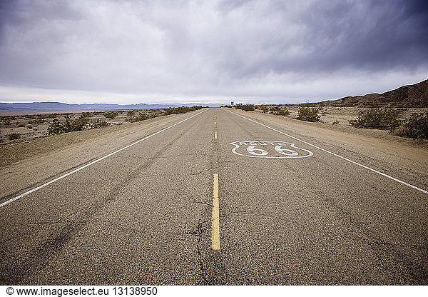 Route 66 sign on desert road against cloudy sky