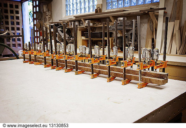 Row bar clamps holding wooden planks on table at workshop