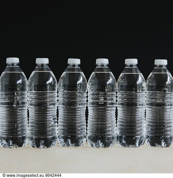 Row of clear  plastic water bottles filled with filtered water in a row  on a black background.