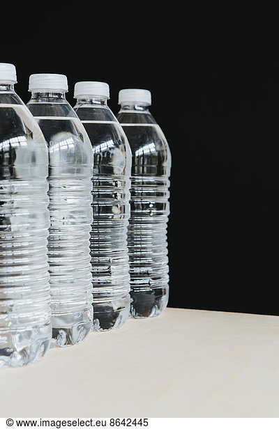 Row of clear  plastic water bottles filled with filtered water in a row. on a black background.