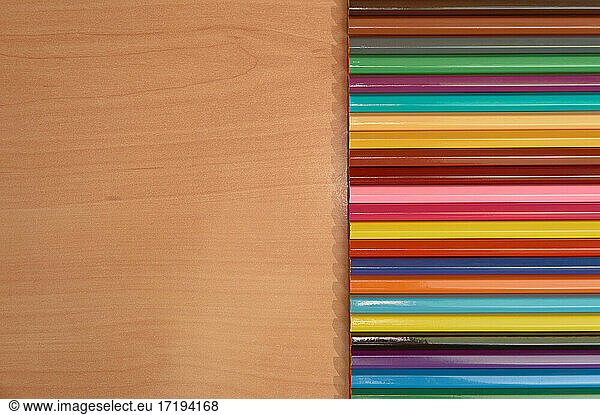 Row of colored pencils on a wooden background.