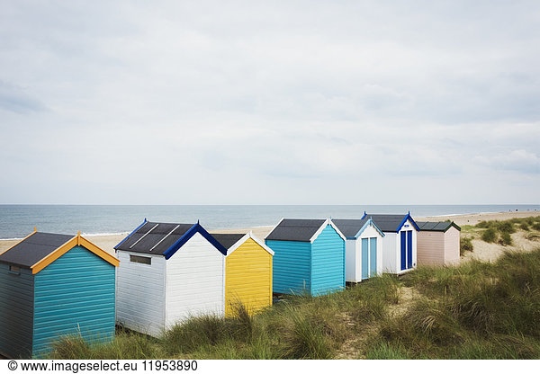 Row of colourful painted beach huts on a sandy beach under a cloudy sky.
