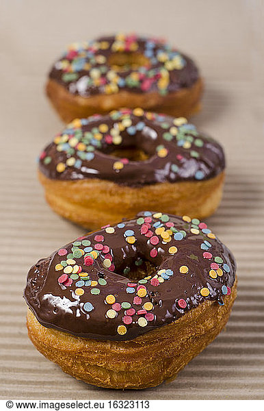 Row of three American cronuts with chocolate icing and sugar confetti