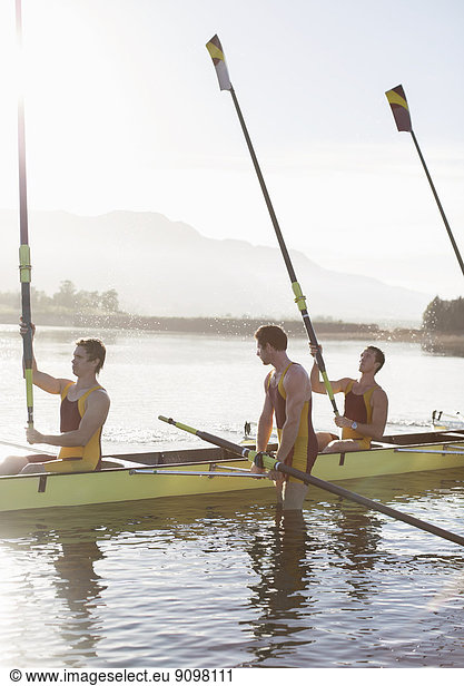Rowing team lifting oars in lake