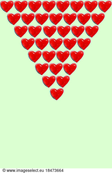 Rows of heart shaped candy flat laid against green background
