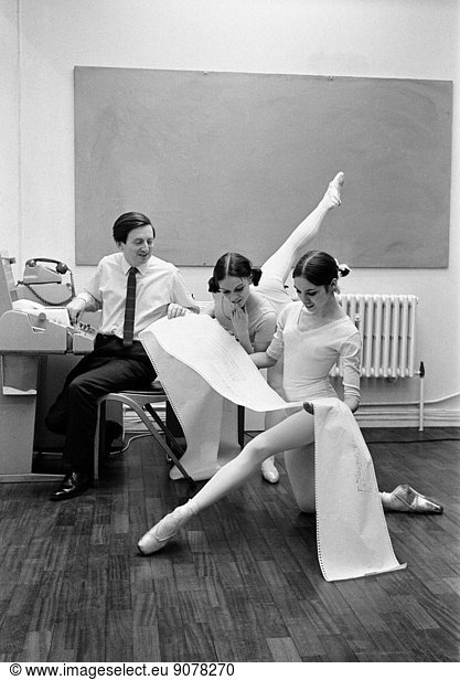 Royal Ballet Company dancers  Lesley Collier aged 22 from Orpington and Marilyn Thompson  21 from San Francisco  study a print out from a teletype machine operated by Mr John Lansdown (left) who has worked a new idea for working out the requirement of computers to the requirements of art. The Computer Arts Society have arranged for Event One to be scheduled at the Royal College of Art where the use of computer programmes covering different arts will be demonstrated. 23rd March 1969.