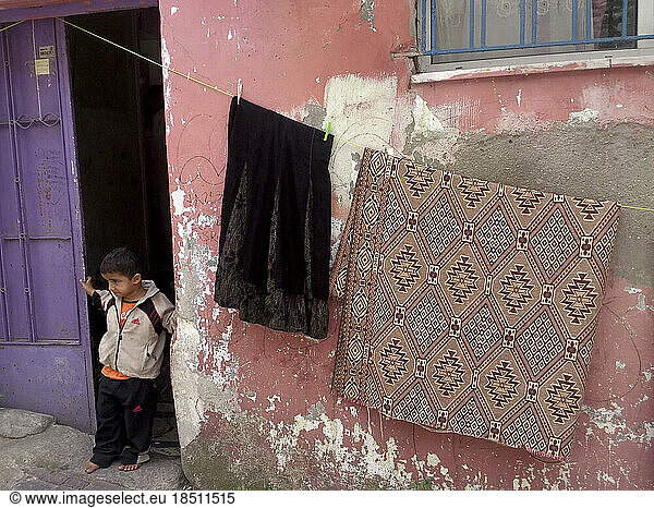 Rugs hanging out to dry on the wall and curious young boy in the