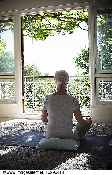Ruhige ältere Frau meditiert an ruhiger Balkontür im Sommer