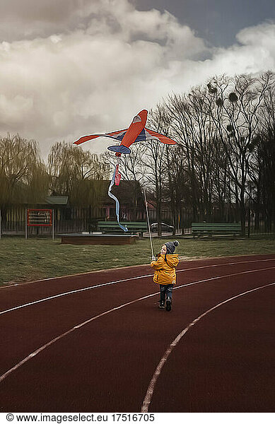 Running boy flying big red airplane kite on treadmil