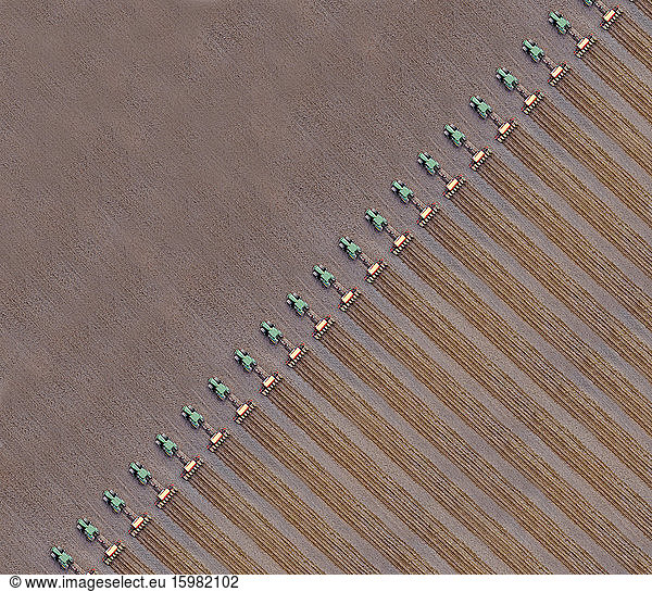Russia  Aerial view of row of tractors plowing brown field