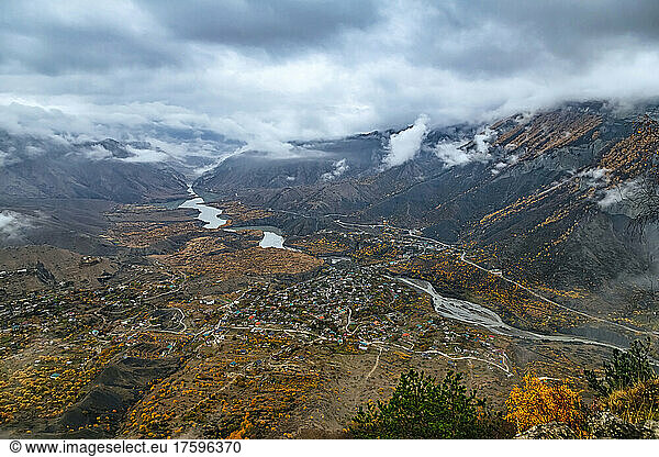 Russia  Dagestan  Gunib  Low clouds over Caucasus Mountains in autumn with village and reservoir in background