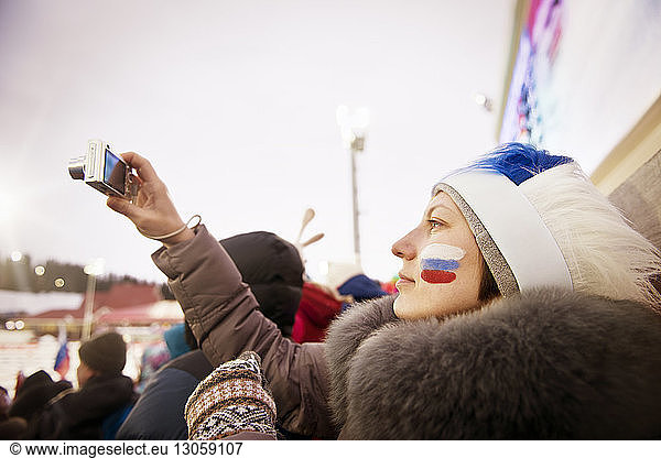 Russian female fan photographing soccer field through camera against clear sky