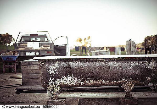 rusty freestanding outdoor tub sits by ute with fire wood on farm