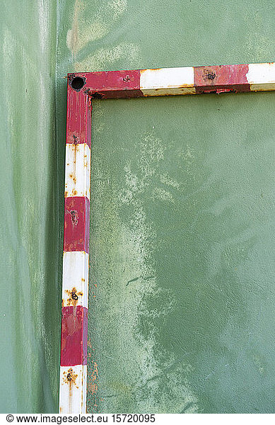 Rusty soccer goal leaning on green wall  partial view