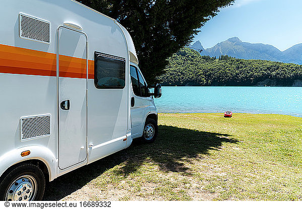 RV motorhome in front of a blue lake with mountains and a red Kayak