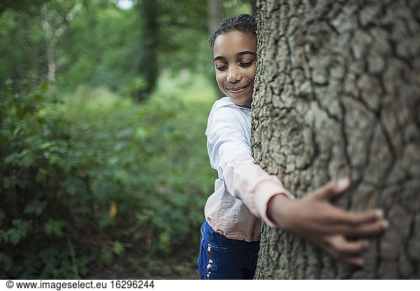 Süßes Mädchen umarmt Baumstamm im Wald