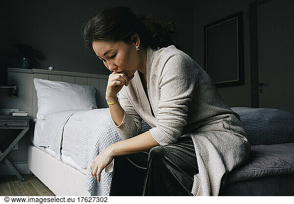 Sad woman sitting with hand on chin in bedroom at home