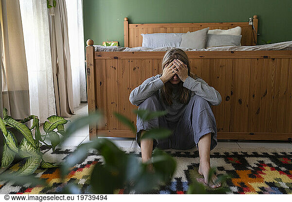 Sad woman with hands covering face sitting at home