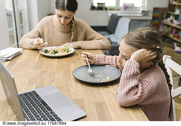 Sad young woman and bored girl eating at home watching laptop