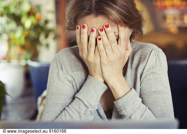 Sad young woman sitting with head in hands at home