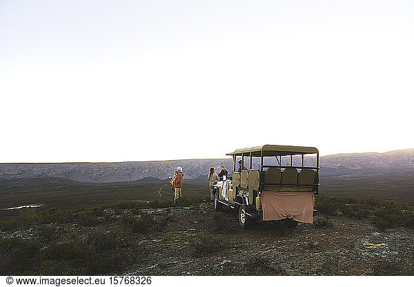 Safari tour group and off-road vehicle on remote hill at sunrise