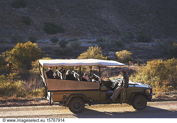 Safari tour guide and group in off-road vehicle on sunny dirt road