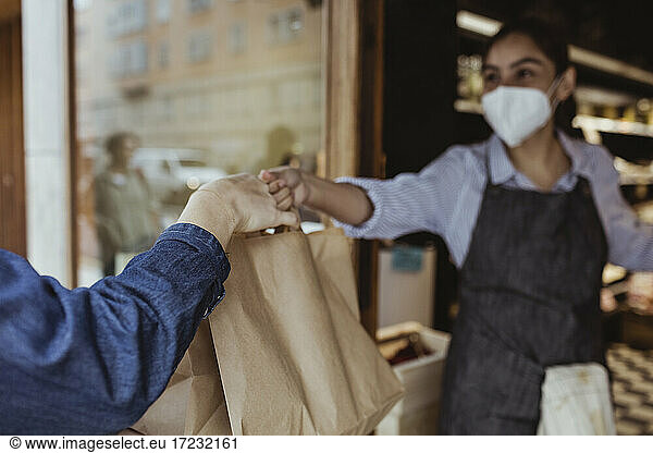 Sales woman giving take away food to customer at deli shop during pandemic