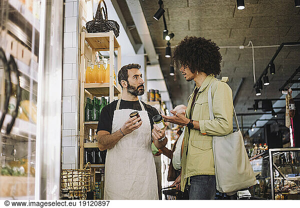 Salesman and young male customer discussing over jars at grocery convenience store